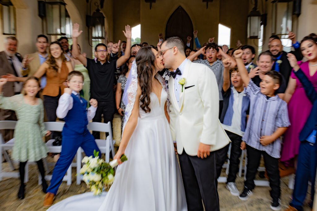 Newlywed couple kissing at Chapel Dulcinea as their family cheers for them. Photo taken by an affordable Chapel Dulcinea photographer