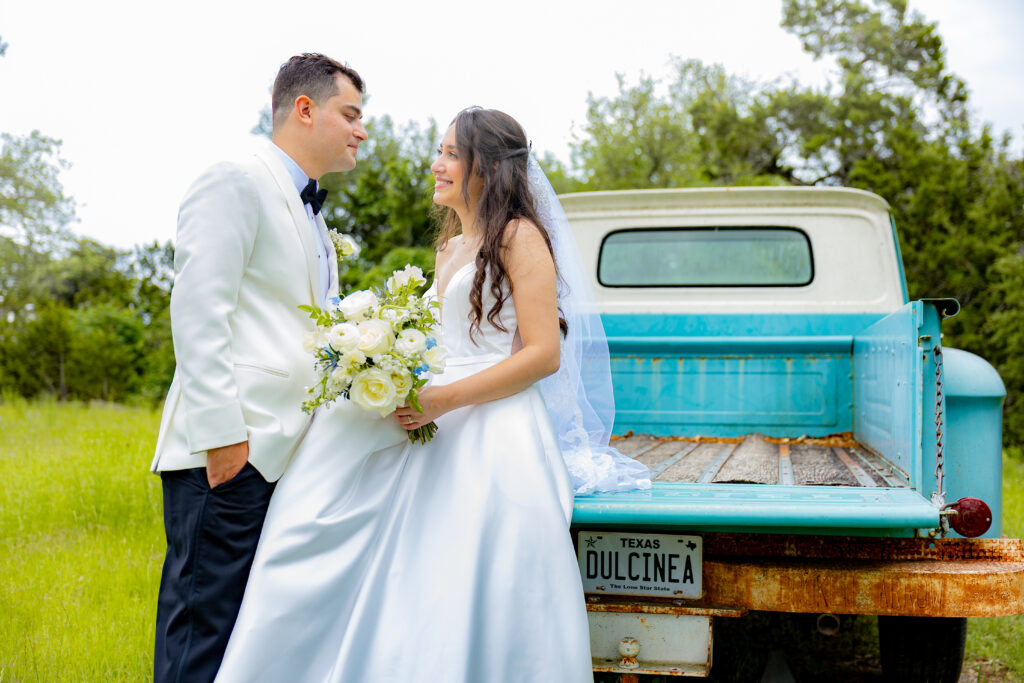 newlywed couple smiling at each other sitting on the infamous blue truck at Chapel Dulcinea.